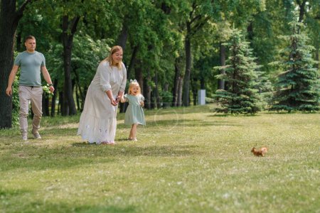 Téléchargez les photos : Heureux famille sur une promenade dans le parc, mère montre à sa fille un écureuil sautant sur l'herbe enfant veut le nourrir - en image libre de droit