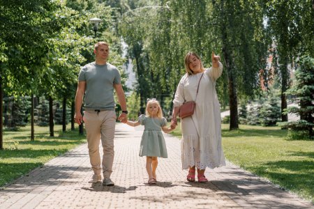 Foto de Niña linda en vestido de verano verde con los padres en el parque de la ciudad a pie estilo de vida familiar de verano Infancia familia feliz cogida de la mano - Imagen libre de derechos