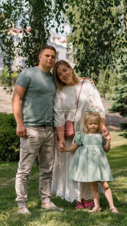 Téléchargez les photos : Portrait d'une jeune famille souriante maman papa et petite fille famille sur une promenade dans le parc enfance heureuse - en image libre de droit