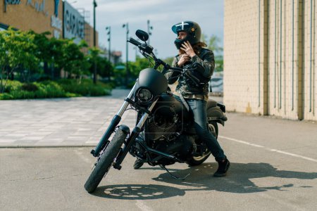 Foto de Brutal motorista pelirrojo se sube a una motocicleta negra antes del inicio de la carrera y se pone un casco de lujuria por la velocidad - Imagen libre de derechos