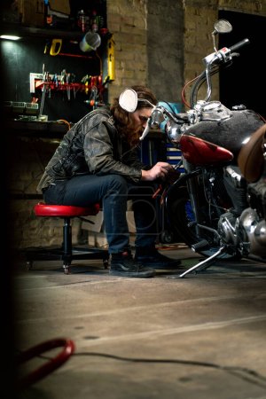 Téléchargez les photos : Atelier de moto authentique créatif Garage rousse barbu motard mécanicien se concentre sur la réparation de la moto - en image libre de droit