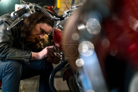 Téléchargez les photos : Atelier de moto authentique créatif Garage rousse barbu motard mécanicien se concentre sur la réparation de la moto - en image libre de droit