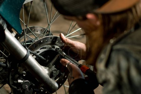 Téléchargez les photos : Atelier de moto authentique créatif Garage motard mécanicien roue réparatrice avec clé close-up - en image libre de droit
