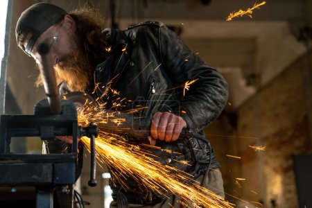Téléchargez les photos : Atelier de moto créatif authentique rousse barbu motard brutal travaille avec scie circulaire Sparks voler de métal chaud - en image libre de droit