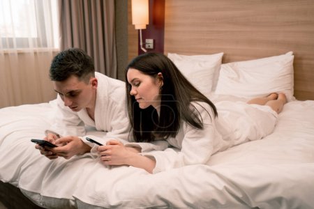 Foto de Pareja joven en la habitación de una habitación de hotel de lujo la gente tiene teléfonos inteligentes en sus manos no se comunican entre sí viajes - Imagen libre de derechos