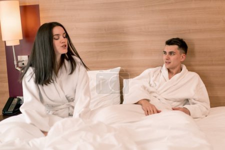 Photo for Portrait of a young couple on their honeymoon in a hotel room lying on bed in white robes quarreling conflict discontent - Royalty Free Image