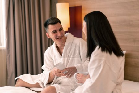 Téléchargez les photos : Jeune couple en lune de miel dans la chambre d'hôtel ayant salle de petit déjeuner boire du café heureux amoureux concept de voyage - en image libre de droit