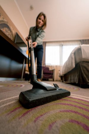 Foto de Muchacha joven trabajadora de limpieza en hotel chica limpieza habitación aspiradora alfombra en habitación de lujo concepto limpieza y hospitalidad - Imagen libre de derechos