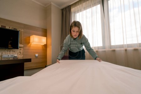 Photo for Portrait of young girl housekeeping worker in hotel girl cleans room makes white clean bed cleanliness hospitality concept - Royalty Free Image
