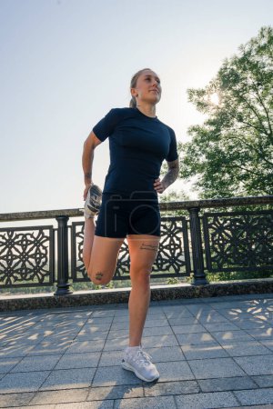 Photo for Fitness young sportswoman girl in the morning doing warm-up leg exercises before training on the street in the city on bridge Sport health - Royalty Free Image