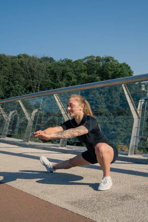 Téléchargez les photos : Fitness jeune fille sportive le matin faire des exercices de jambes échauffement avant l'entraînement dans la rue dans la ville sur le pont Sport santé - en image libre de droit