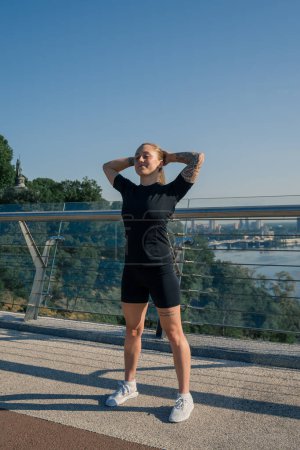 Photo for Fitness young sportswoman girl in morning doing warm-up exercises before training on the street in the city on the bridge Sport health - Royalty Free Image