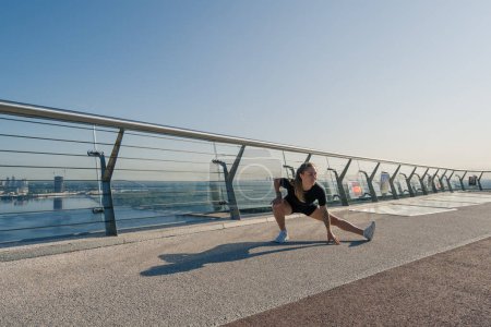 Téléchargez les photos : Fitness jeune fille sportive le matin faire des exercices de jambes échauffement avant l'entraînement dans la rue dans la ville sur le pont Sport santé - en image libre de droit