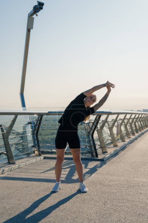 Foto de Chica deportista joven fitness en la mañana haciendo ejercicios de calentamiento antes de entrenar en la calle en la ciudad en el puente Salud deportiva - Imagen libre de derechos