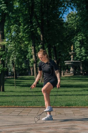 Photo for Fitness young sportsman girl with tattoos in the morning doing sports jumping rope during exercise outdoors in the city in health park - Royalty Free Image