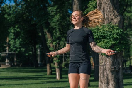 Foto de Chica deportista joven fitness con tatuajes en la mañana haciendo deportes saltar la cuerda durante el ejercicio al aire libre en la ciudad en el parque de salud - Imagen libre de derechos