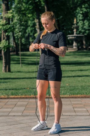 Photo for Fitness young sportsman girl with tattoos in the morning doing sports jumping rope during exercise outdoors in the city in health park - Royalty Free Image