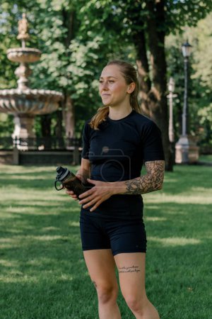 Téléchargez les photos : Portrait de jeune fille sportive satisfaite tenant la bouteille d'eau à l'extérieur après l'entraînement concept de mode de vie sain parc - en image libre de droit