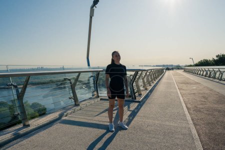 Photo for Fitness young sportswoman girl in morning doing warm-up exercises before training on the street in the city on the bridge Sport health - Royalty Free Image