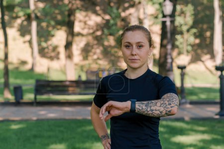 Photo for Portrait of a young sportswoman checking the time and pulse on a smart watch after a workout in the park healthy lifestyle concept - Royalty Free Image