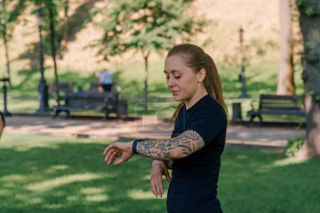 Téléchargez les photos : Portrait d'une jeune sportive vérifiant le temps et le pouls d'une montre intelligente après une séance d'entraînement dans le parc concept de mode de vie sain - en image libre de droit
