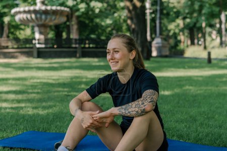Téléchargez les photos : Portrait de jeune fille sportive satisfaite reposant sur l'eau potable tapis de sport à l'extérieur après l'entraînement concept de mode de vie sain parc - en image libre de droit