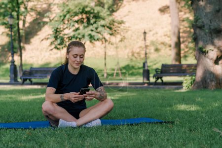 Foto de Retrato de una joven atleta en una alfombra deportiva descansando después de entrenar en el parque con un smartphone en sus manos el concepto de estilo de vida saludable - Imagen libre de derechos