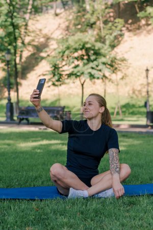 Foto de Retrato de una joven atleta en una alfombra deportiva descansando después de un entrenamiento en el parque tomando una selfie en un teléfono inteligente el concepto de estilo de vida saludable - Imagen libre de derechos