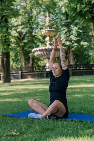 Foto de Retrato de una joven deportista meditando haciendo yoga en una esterilla deportiva al aire libre mientras hace ejercicio el concepto de estilo de vida saludable del parque - Imagen libre de derechos