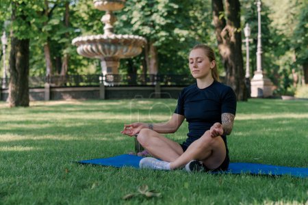 Photo for Portrait of young sporty girl meditating doing yoga on sports mat outdoors while exercising park healthy lifestyle concept - Royalty Free Image