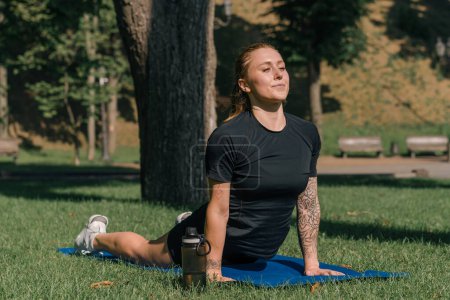 Téléchargez les photos : Jeune fille sportive faisant des exercices physiques sur un tapis de sport yoga entraînement en plein air dans le parc sur l'herbe concept de mode de vie sain - en image libre de droit