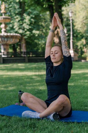 Téléchargez les photos : Portrait de jeune fille sportive méditant faire du yoga sur tapis de sport à l'extérieur tout en exerçant concept de style de vie sain parc - en image libre de droit