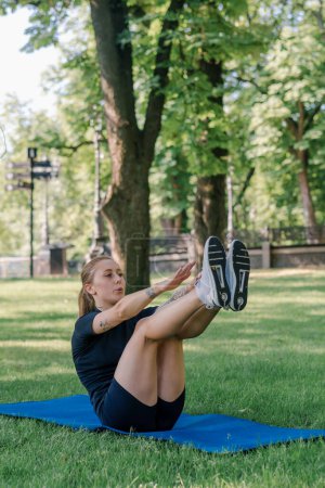 Photo for Portrait of a young sporty girl doing abdominal exercises on a sports mat outdoors while exercising in park healthy lifestyle concept - Royalty Free Image