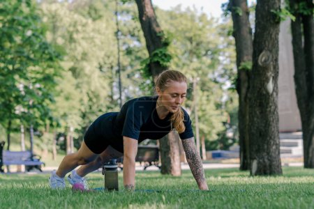 Foto de Retrato de una joven deportista satisfecha haciendo flexiones al aire libre mientras hace ejercicio en el parque concepto de estilo de vida saludable - Imagen libre de derechos