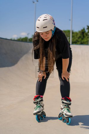 Foto de Retrato de niña en casco protector y patines cansados después de patinar y acrobacias en el parque de skate rampa después de la competencia - Imagen libre de derechos