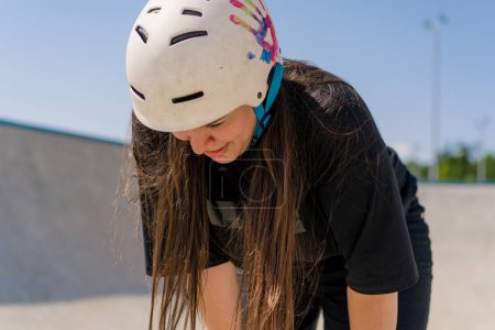 Photo for Portrait of young girl in protective helmet and roller skates tired after skating and stunts on ramp skate park after competition - Royalty Free Image