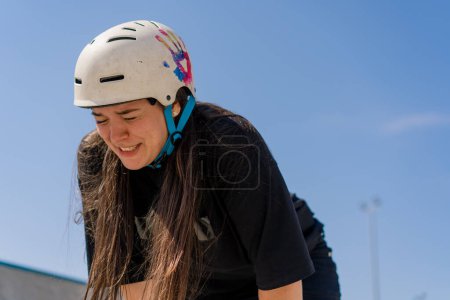 Photo for Portrait of young girl in protective helmet and roller skates tired after skating and stunts on ramp skate park after competition - Royalty Free Image