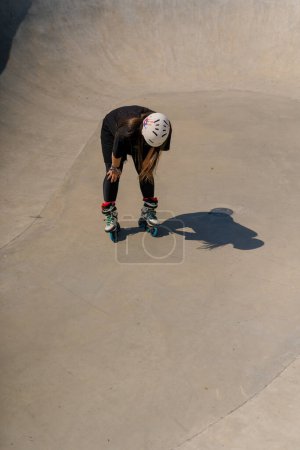 Foto de Chica en casco de seguridad y patines cansados después de patinar y acrobacias rampa en skate park después de la competencia - Imagen libre de derechos