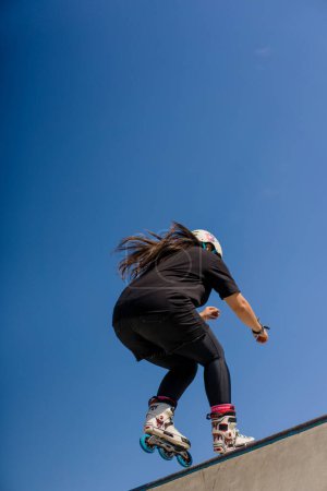 Photo for Young skilled woman rollerblading and jumping on the ramp in the skate park outside Practicing her tricks or technique of rollerblading competition - Royalty Free Image
