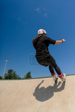 Foto de Joven mujer calificada patinaje y saltar en la rampa en el parque de skate fuera Practicando sus trucos o técnica de competencia patinaje - Imagen libre de derechos
