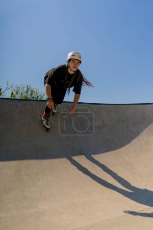Téléchargez les photos : Jeune femme qualifiée roller et sauter sur la rampe dans le skate park à l'extérieur Pratiquer ses tours ou la technique de la compétition de roller - en image libre de droit