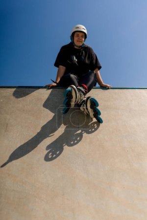 Photo for Young hipster girl in protective helmet roller skates sitting in skate park before skating and doing tricks street extreme sport - Royalty Free Image