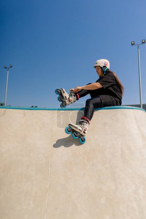 Photo for Young hipster girl in protective helmet on roller skates tying laces skate park before skating street extreme sport - Royalty Free Image