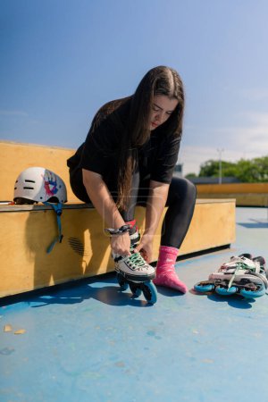 Foto de Joven hipster chica usando patines atando cordones skate park antes de patinar calle deporte extremo - Imagen libre de derechos