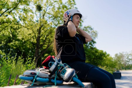 Photo for Portrait of a young smiling hipster girl in a skate park wearing a protective helmet before starting to skate roller skates in background - Royalty Free Image