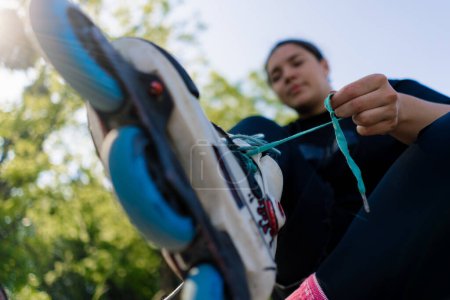 Foto de Joven hipster chica usando patines atando cordones en skate park antes de patinar calle extrema deporte primer plano de las piernas - Imagen libre de derechos