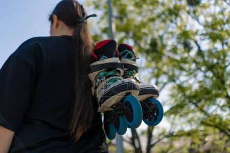Photo for Young hipster girl carries roller skates before starting training lesson sports field street sport back view - Royalty Free Image