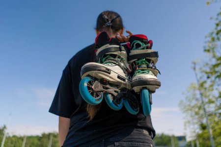 Photo for Young hipster girl carries roller skates before starting training lesson sports field street sport back view - Royalty Free Image