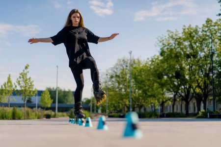 Photo for Sporty girl practicing tricks on roller skates in park on city background enjoying roller skating lesson with chips closeup Street sports concept - Royalty Free Image