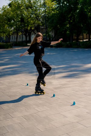 Foto de Chica deportiva practicando trucos en patines en el parque en el fondo de la ciudad disfrutando de clases de patinaje sobre ruedas con patatas fritas primer plano concepto de deportes callejeros - Imagen libre de derechos